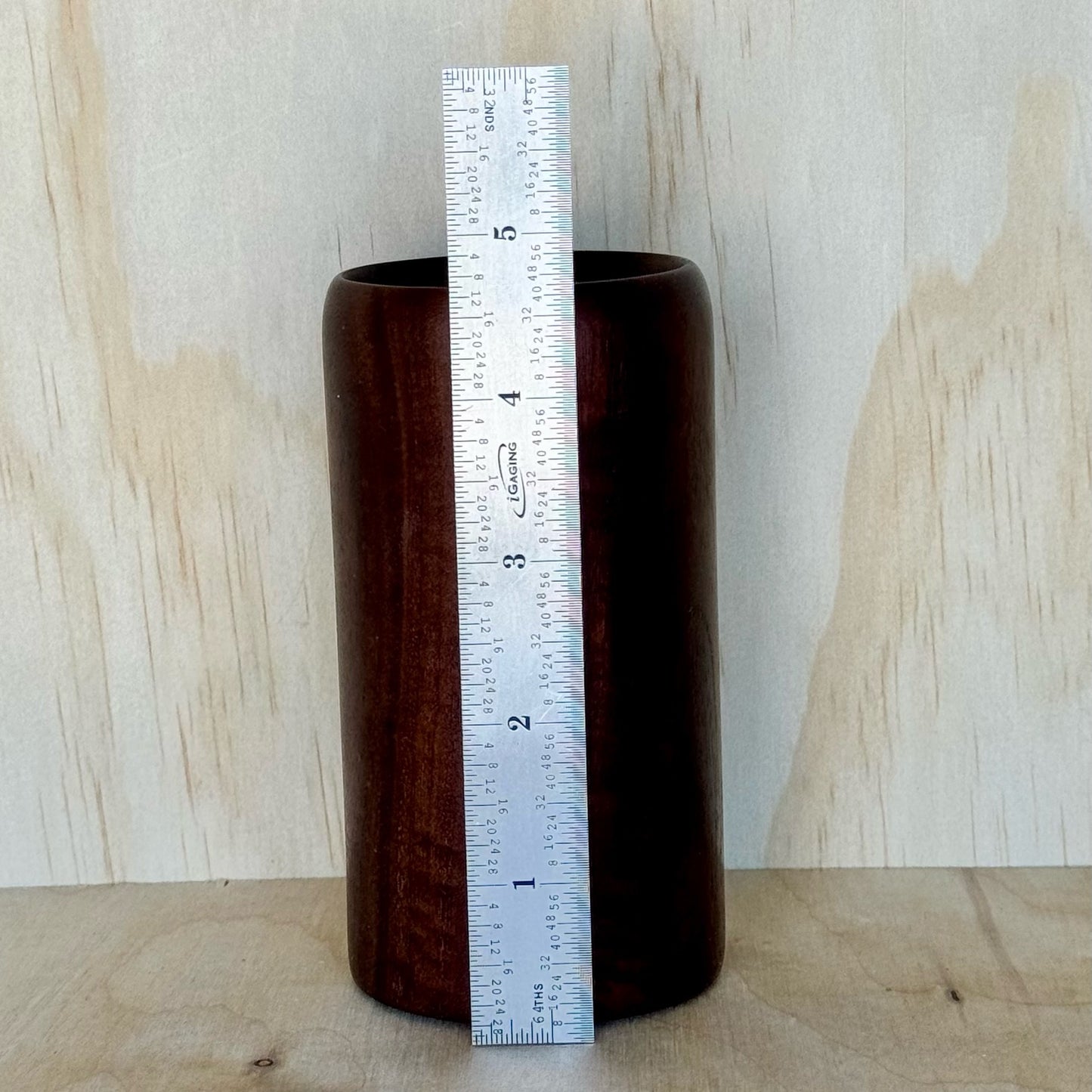 Wooden tumbler on a wooden surface with a light wood panel background and a ruler showing that it is 4-3/5 inches tall
