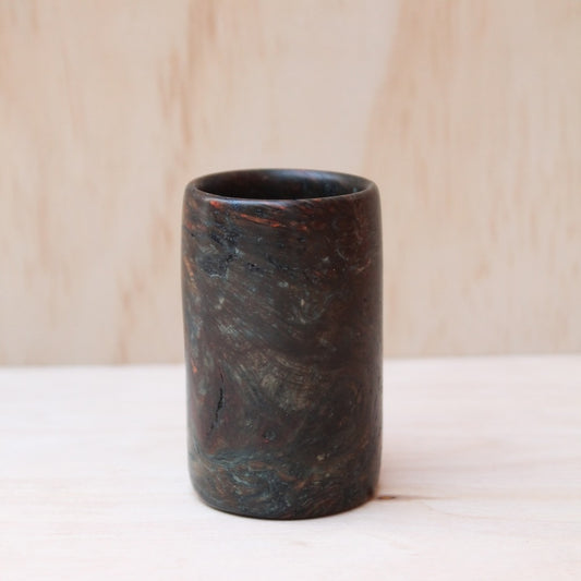 dark brown wooden shot glass made of exotic burl wood on a light wooden background.