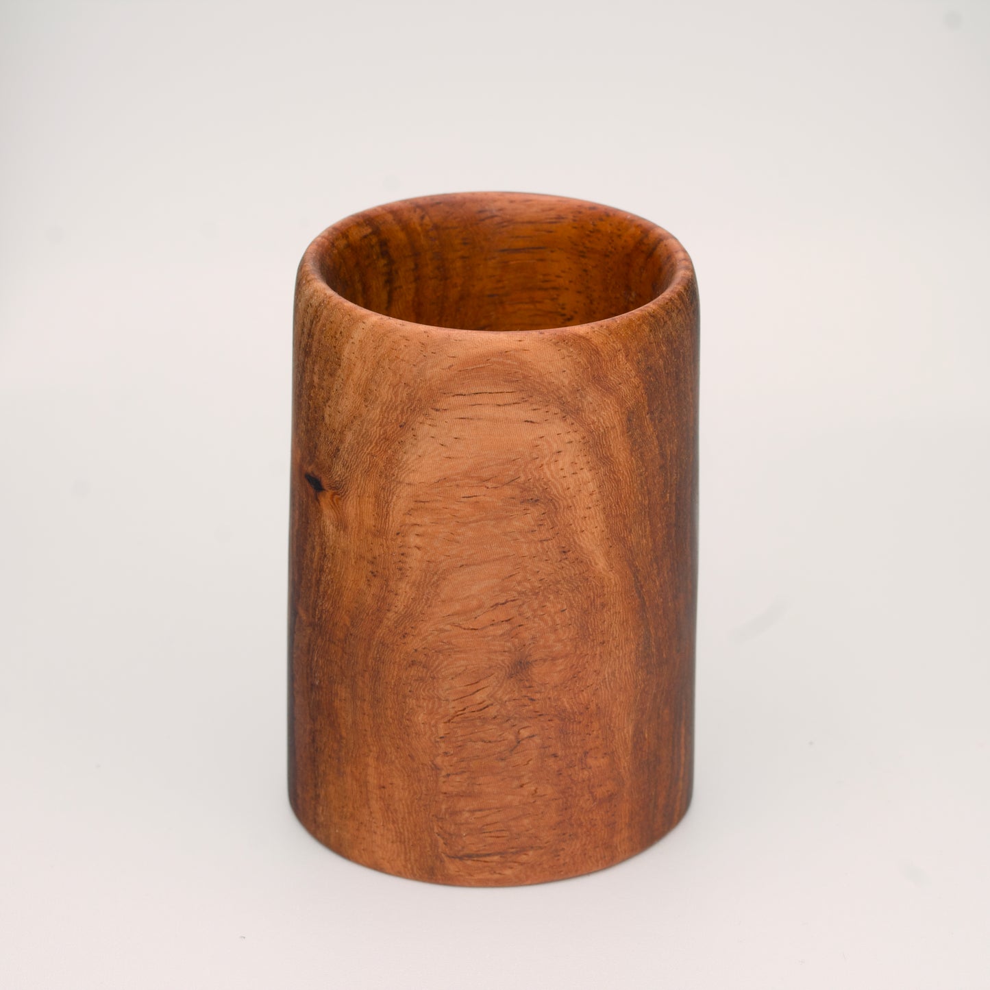 wooden shot glass with deep chocolate tones with light brown stripes on a light wooden background