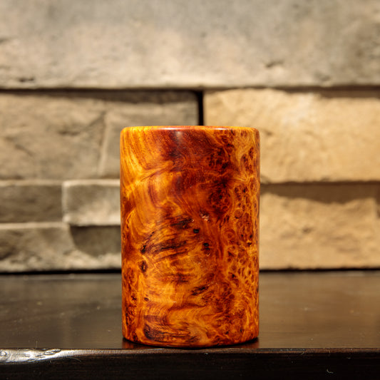 Side view of the Amboyna burl shot glass showing sweeping golden grain, darker reddish-brown swirls, and small burl eyes.