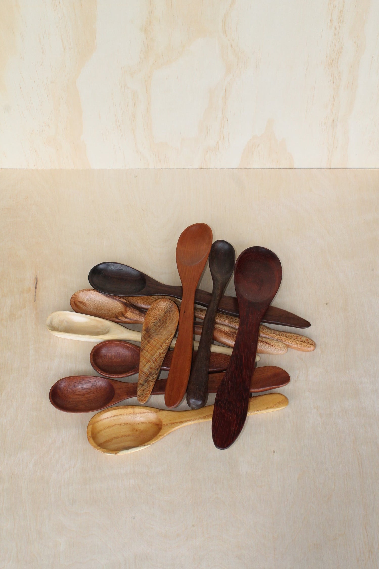 variety of colors of hand made wooden spoons and spatulas stacked on a light wooden background