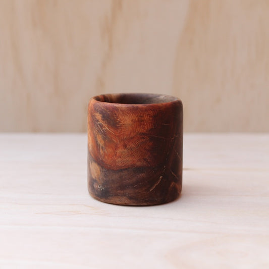 Wooden cup with a natural finish on a light background. pattern shows swirling interplay of deep chocolate browns, golden streaks, and reddish undertones