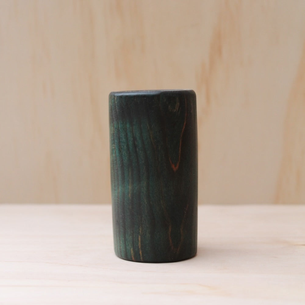 wooden shot glass made of ash wood dyed in blue on a light wood background. The pattern of wood shows hints of light brown