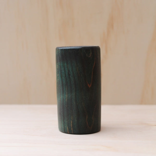 wooden shot glass made of ash wood dyed in blue on a light wood background. The pattern of wood shows hints of light brown