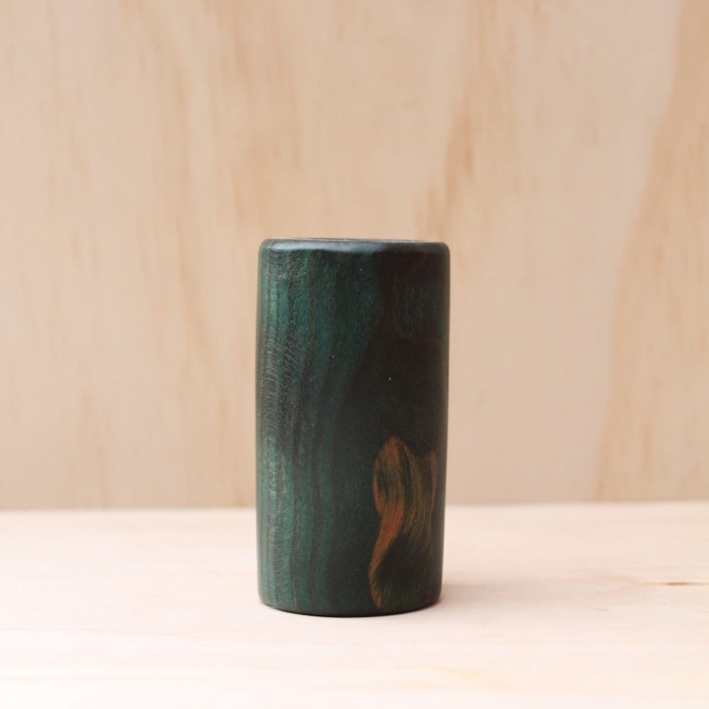 wooden shot glass made of ash wood dyed in blue on a light wood background. The pattern of wood shows hints of light brown