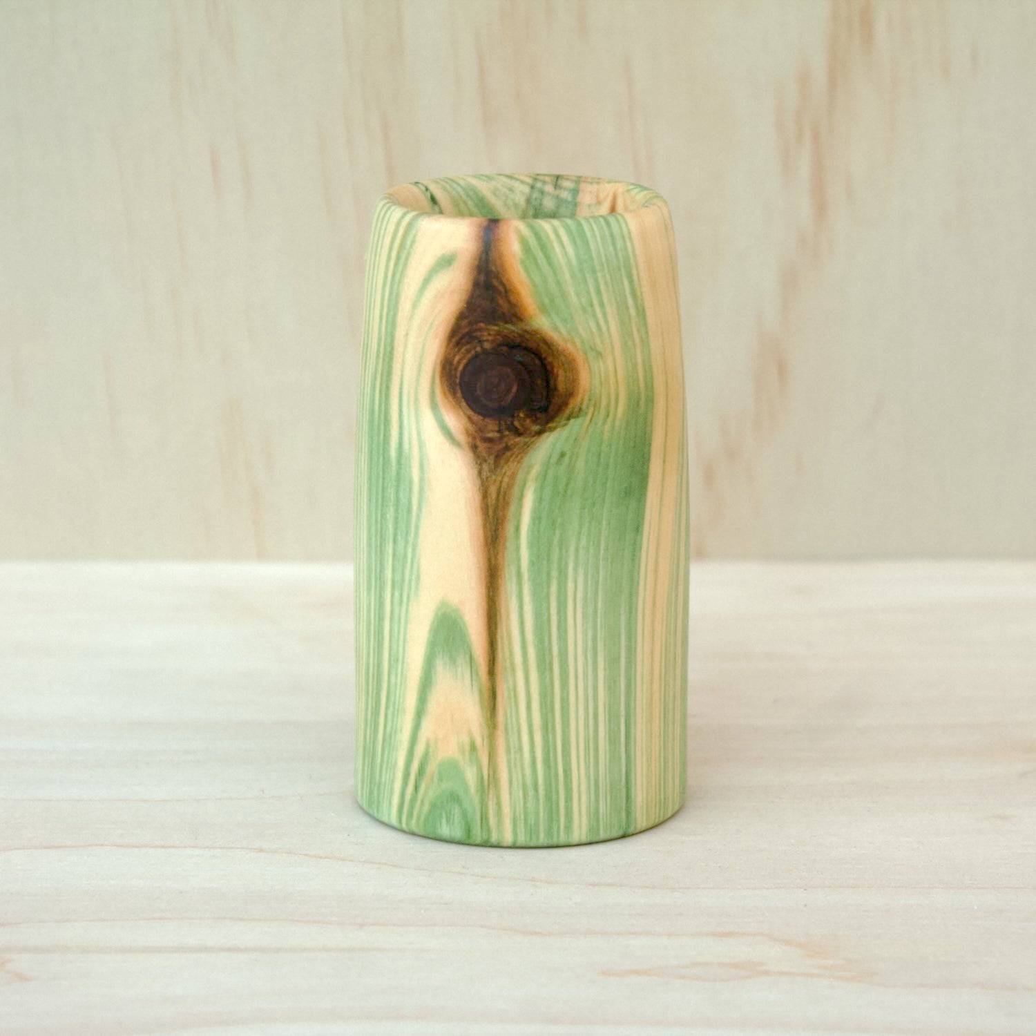Wooden cup with green and brown marbled pattern on a wooden surface