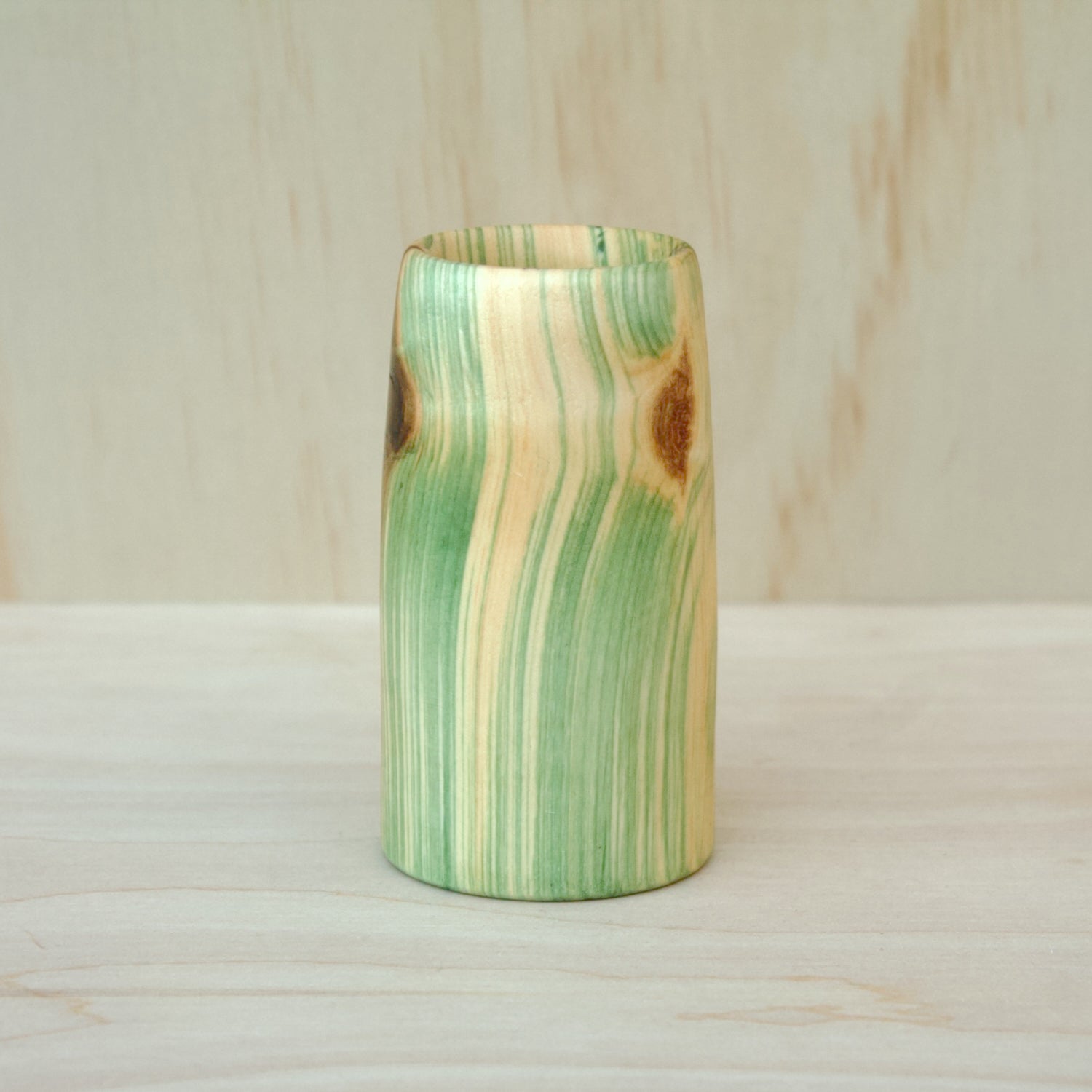 Wooden glass with green and brown striped pattern on a wooden surface