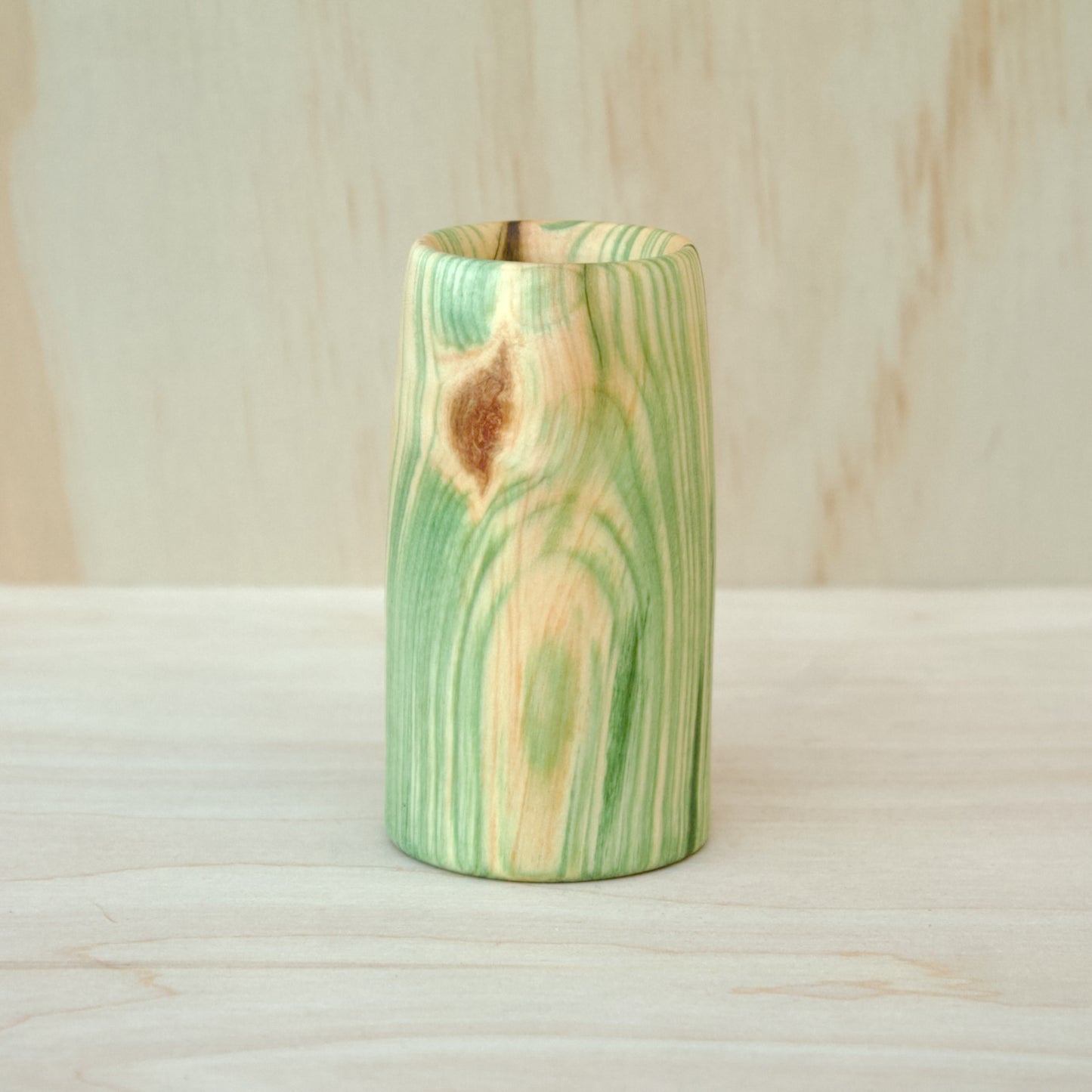 Wooden vase with green and brown patterns on a wooden surface