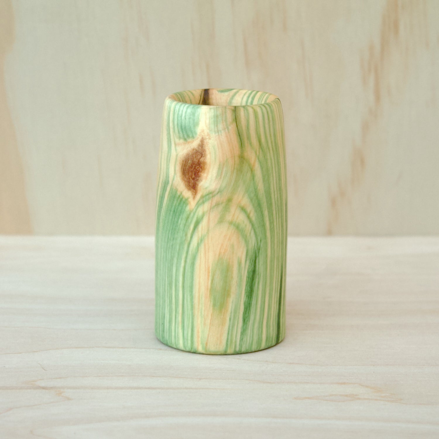 Wooden vase with green and brown patterns on a wooden surface