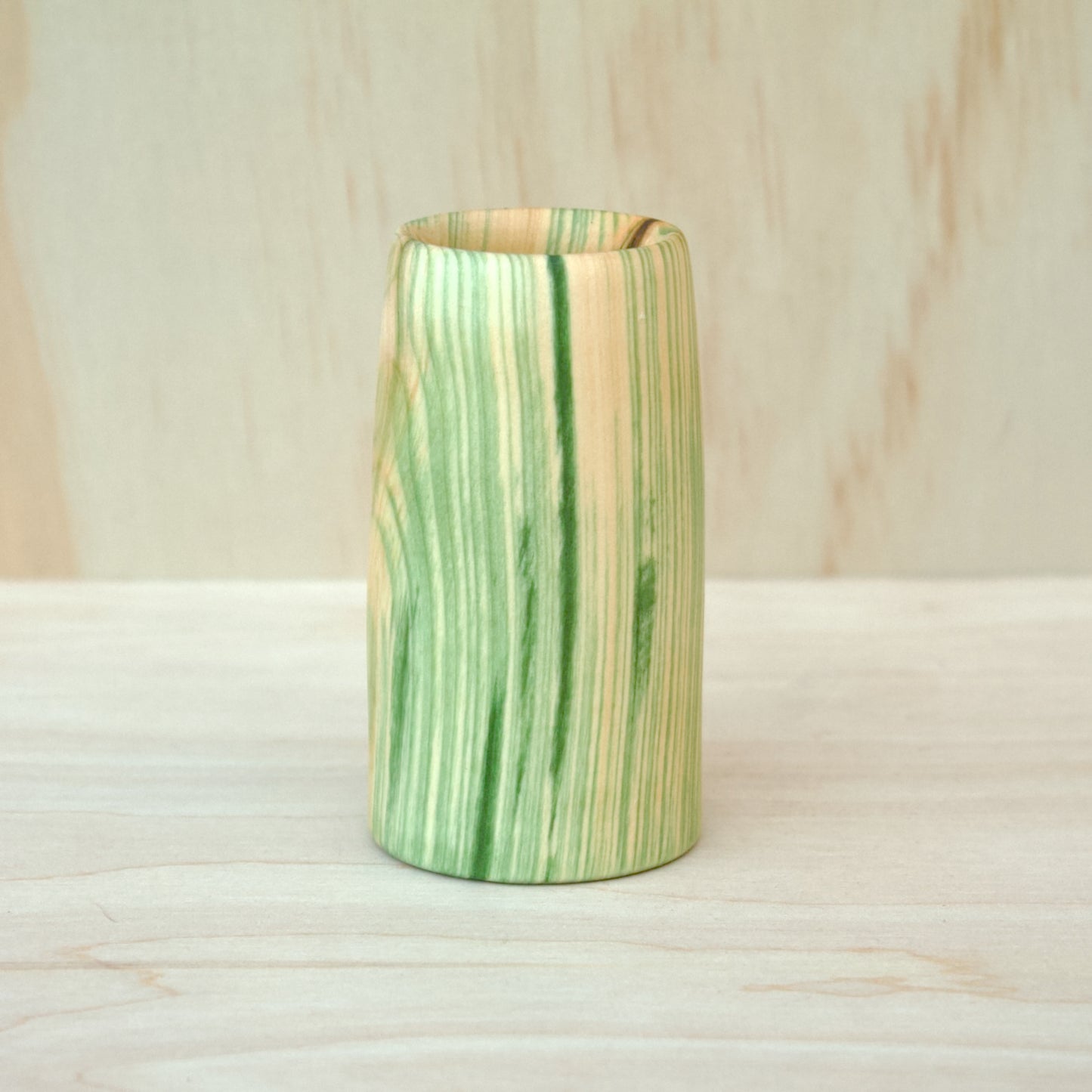 Green and brown striped wooden cup on a wooden surface