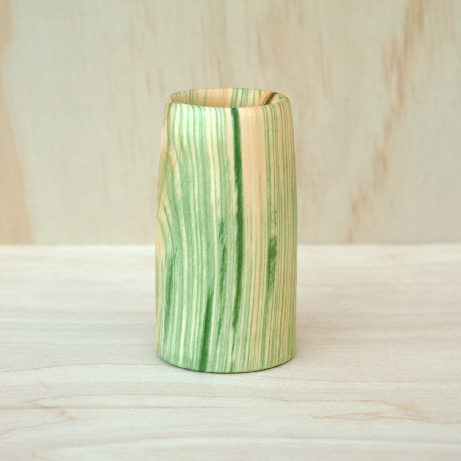 Green and brown striped wooden cup on a wooden surface