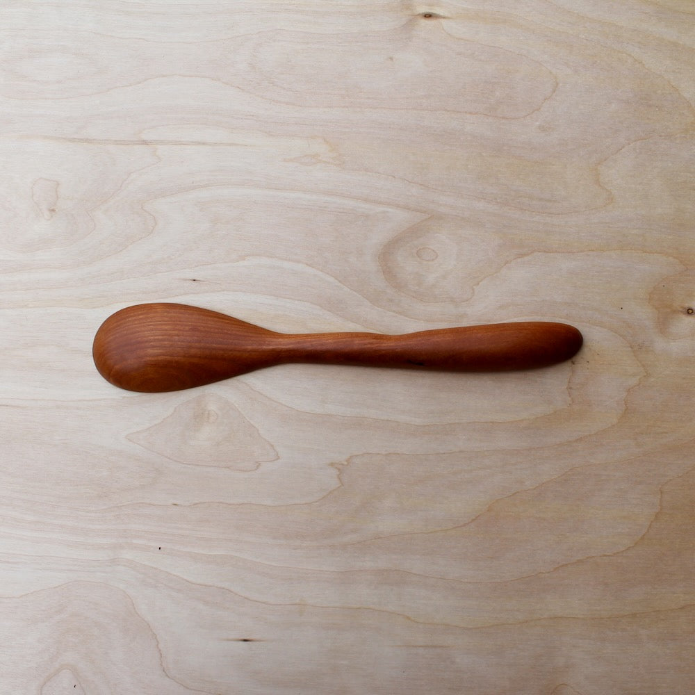 back of a hand made wooden spatula, made with cherry wood, on a light wooden background