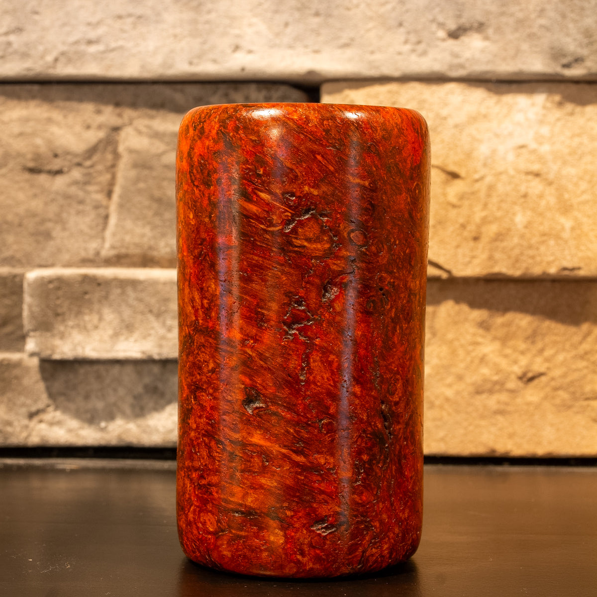 Amboyna Burl wood shot glass against stone fire place mantel. 