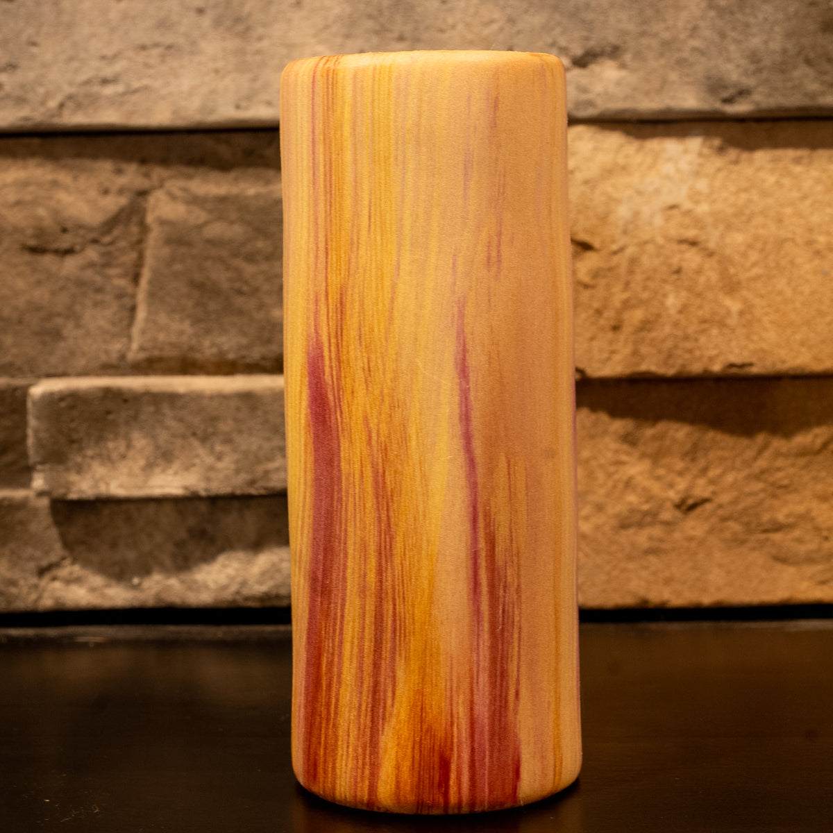 Tall rainbow colored aspen wood shot glass against stone fireplace background.