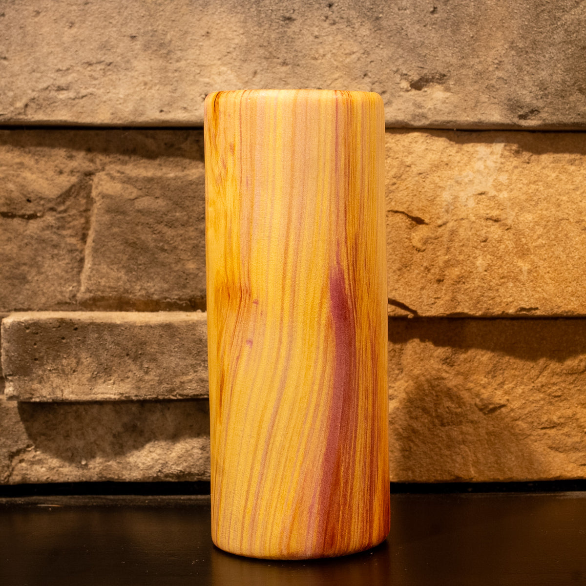 Tall rainbow colored aspen wood shot glass against stone fireplace background.