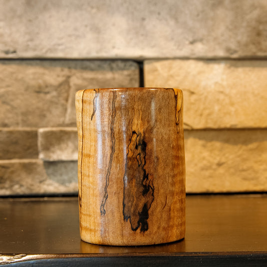 Spalted maple shot glass with a large dark spalted area against warm golden and brown wood.