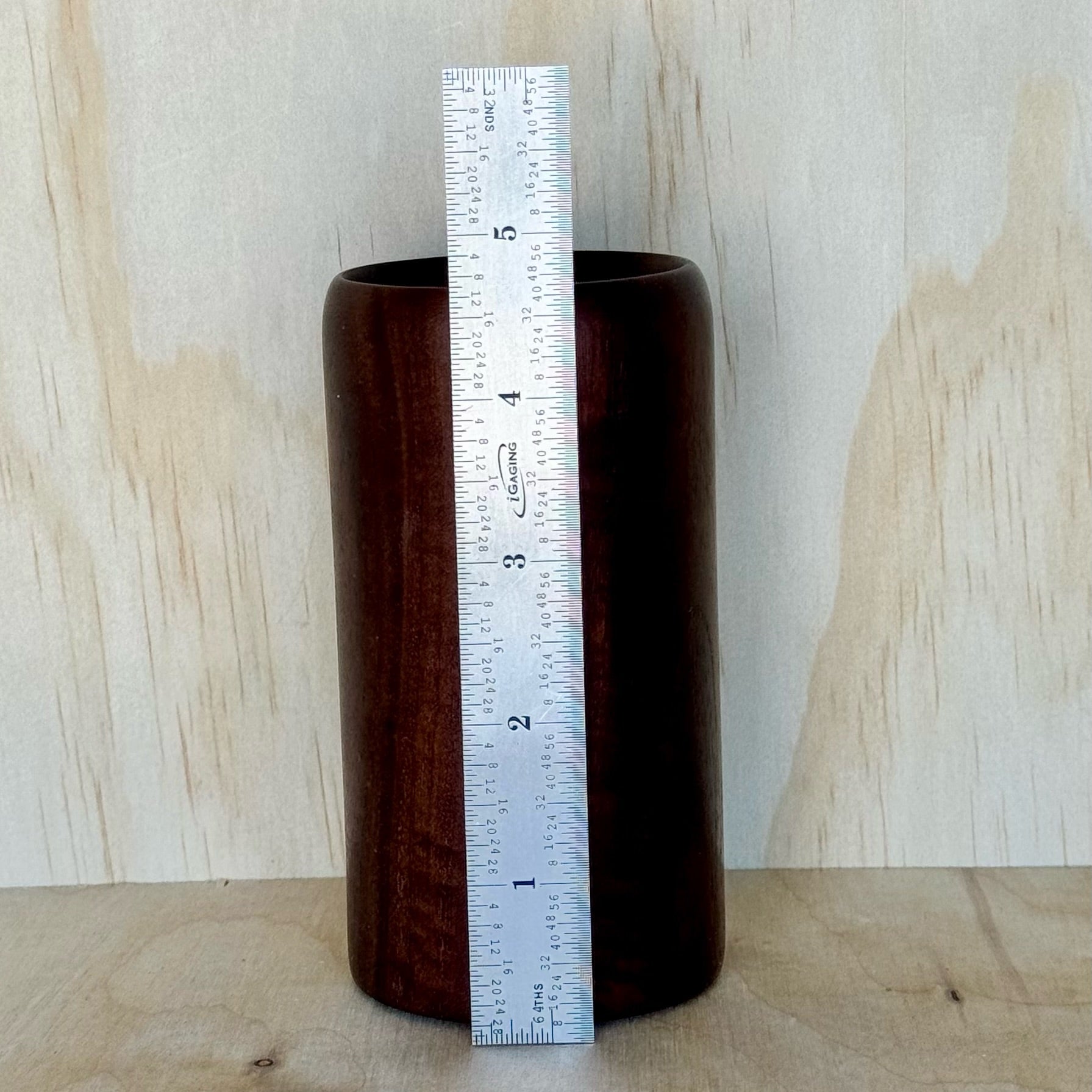 Wooden tumbler on a wooden surface with a light wood panel background and a ruler showing that it is 4-3/5 inches tall