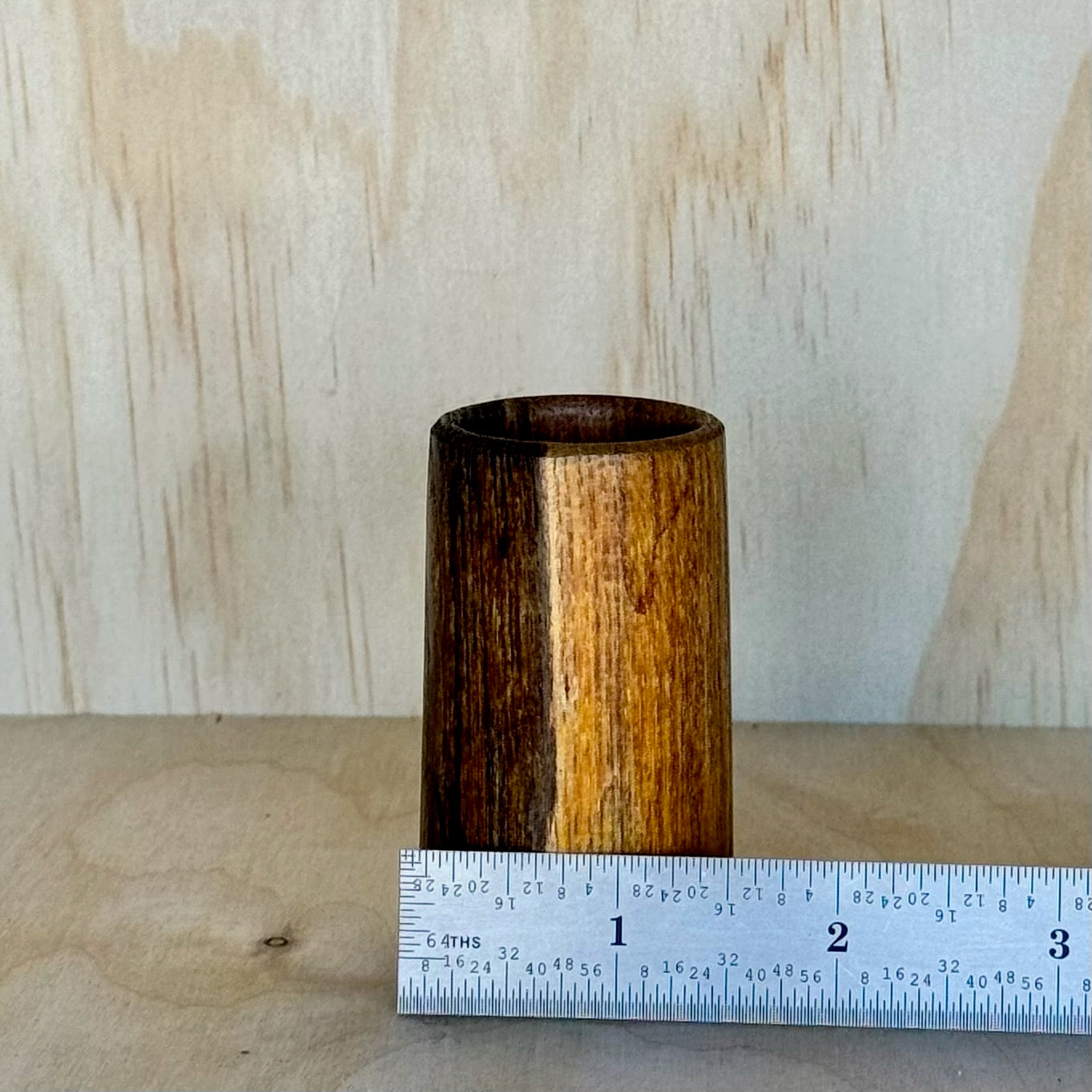 Wooden shot glass on a wooden surface with a light background and a ruler showing that it is 1.5 inches wide