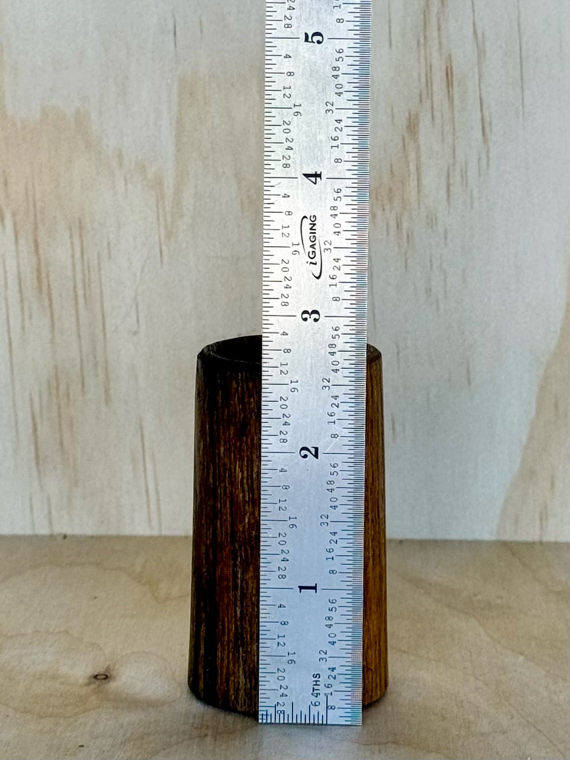Wooden shot glass on a wooden surface with a light background and a ruler showing it is 2.5 inches tall