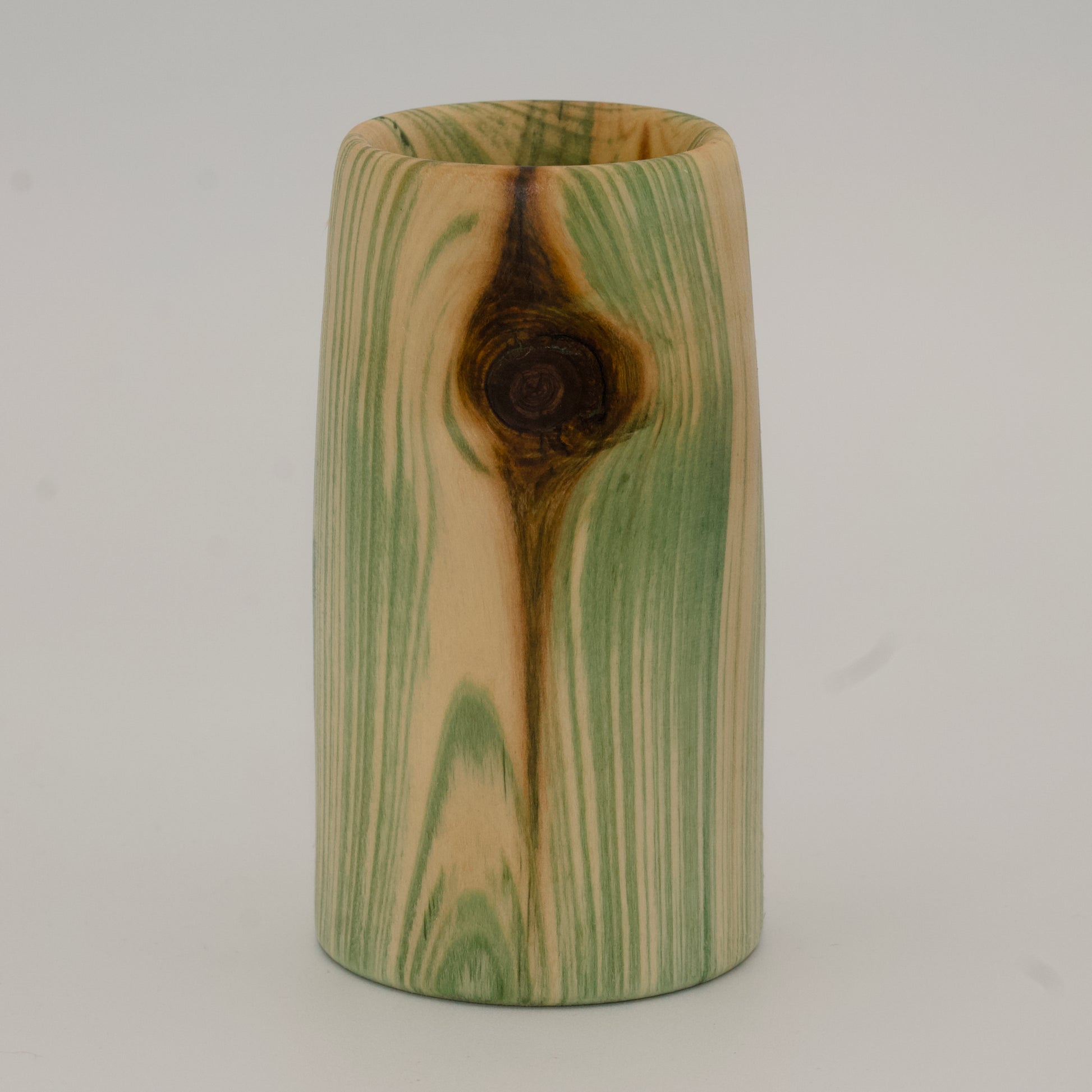 Wooden cup with green and brown marbled pattern on a wooden surface