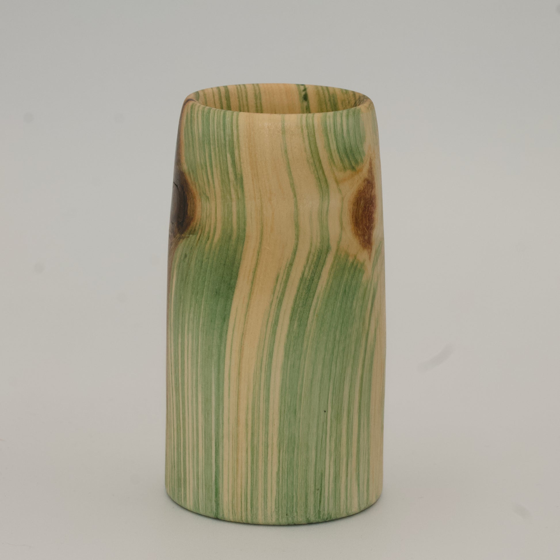 Wooden cup with green and brown marbled pattern on a wooden surface