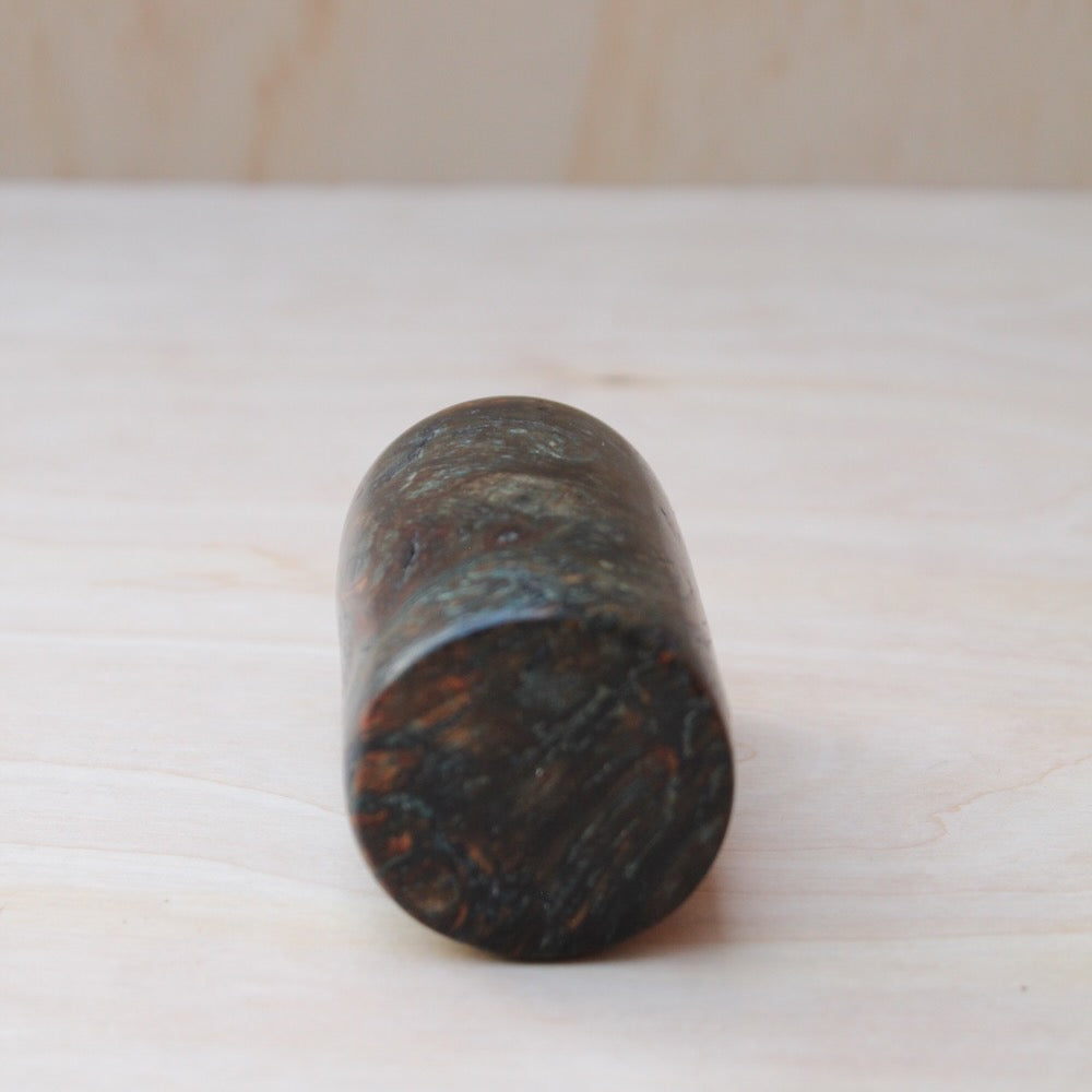 bottom view of dark brown and blue wooden shot glass made of exotic burl wood on a light wooden background. The wooden pattern is consists of dark blue and golden accent
