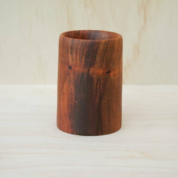 foodsafe, wooden shot glass with deep chocolate tones with light brown stripes on a light wooden background
