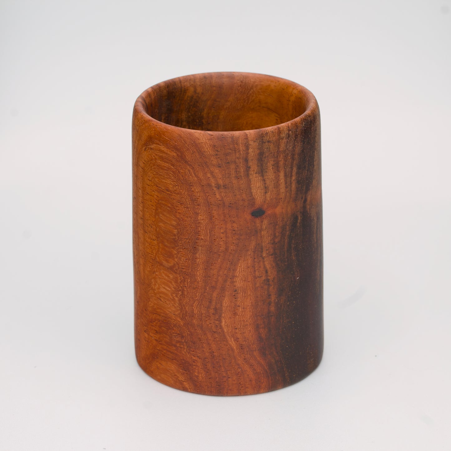 wooden shot glass with deep chocolate tones with light brown stripes on a light wooden background