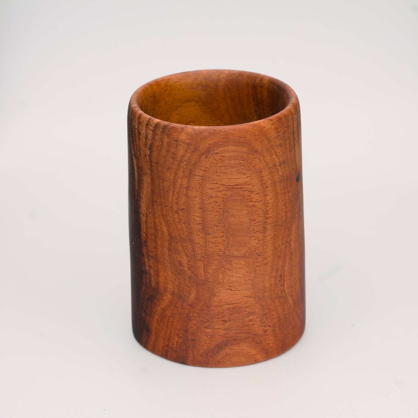 wooden shot glass with deep chocolate tones with light brown stripes on a light wooden background