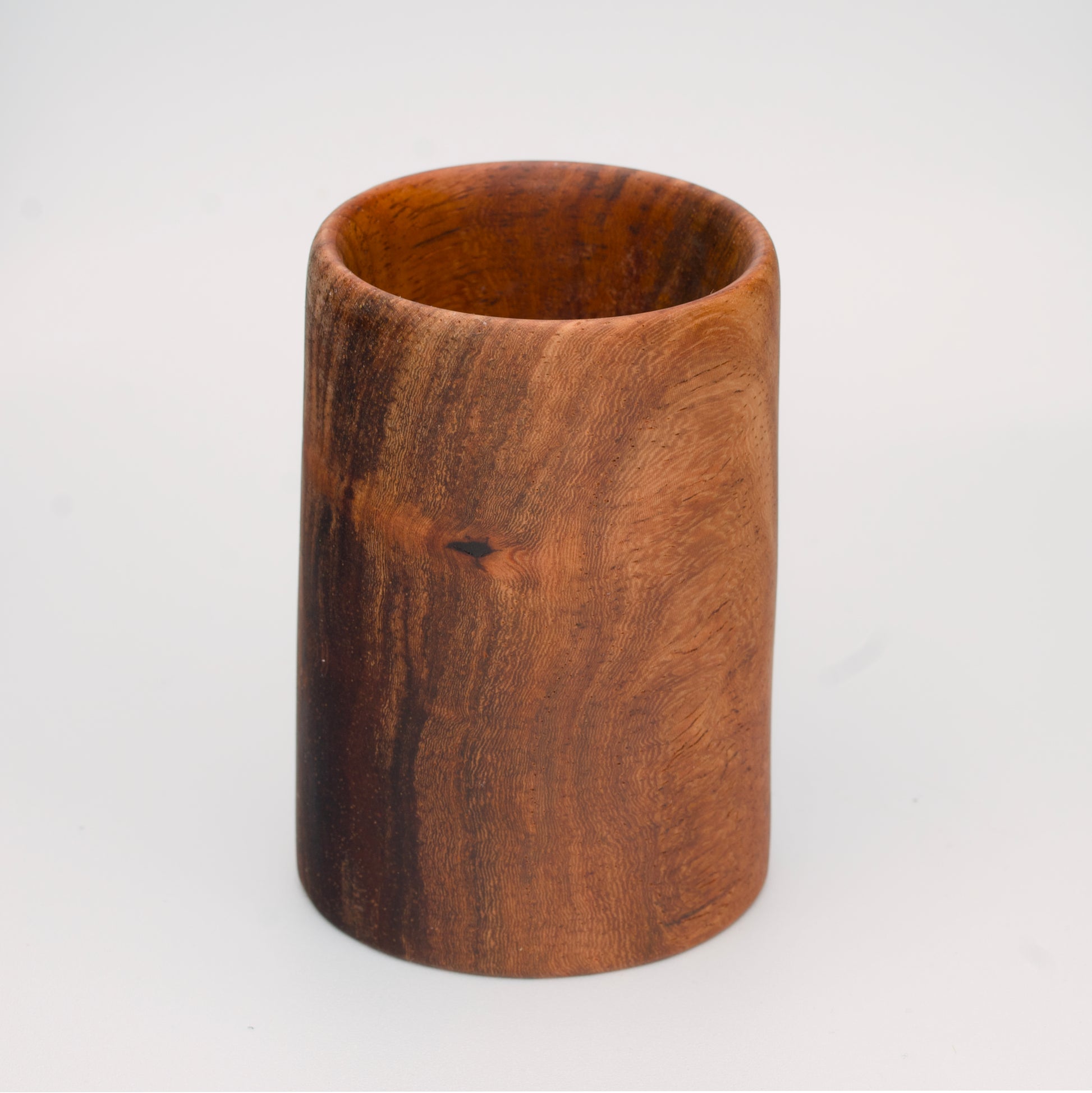 wooden shot glass with deep chocolate tones with light brown stripes on a light wooden background