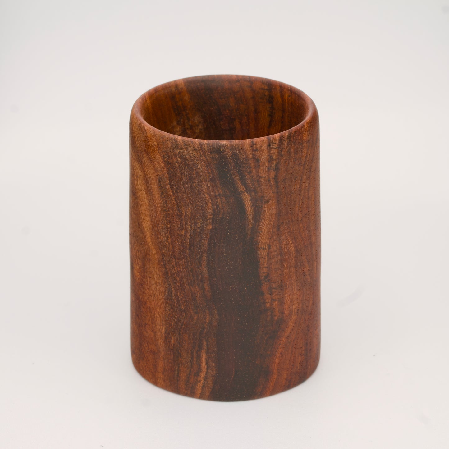 wooden shot glass with deep chocolate tones with light brown stripes on a light wooden background