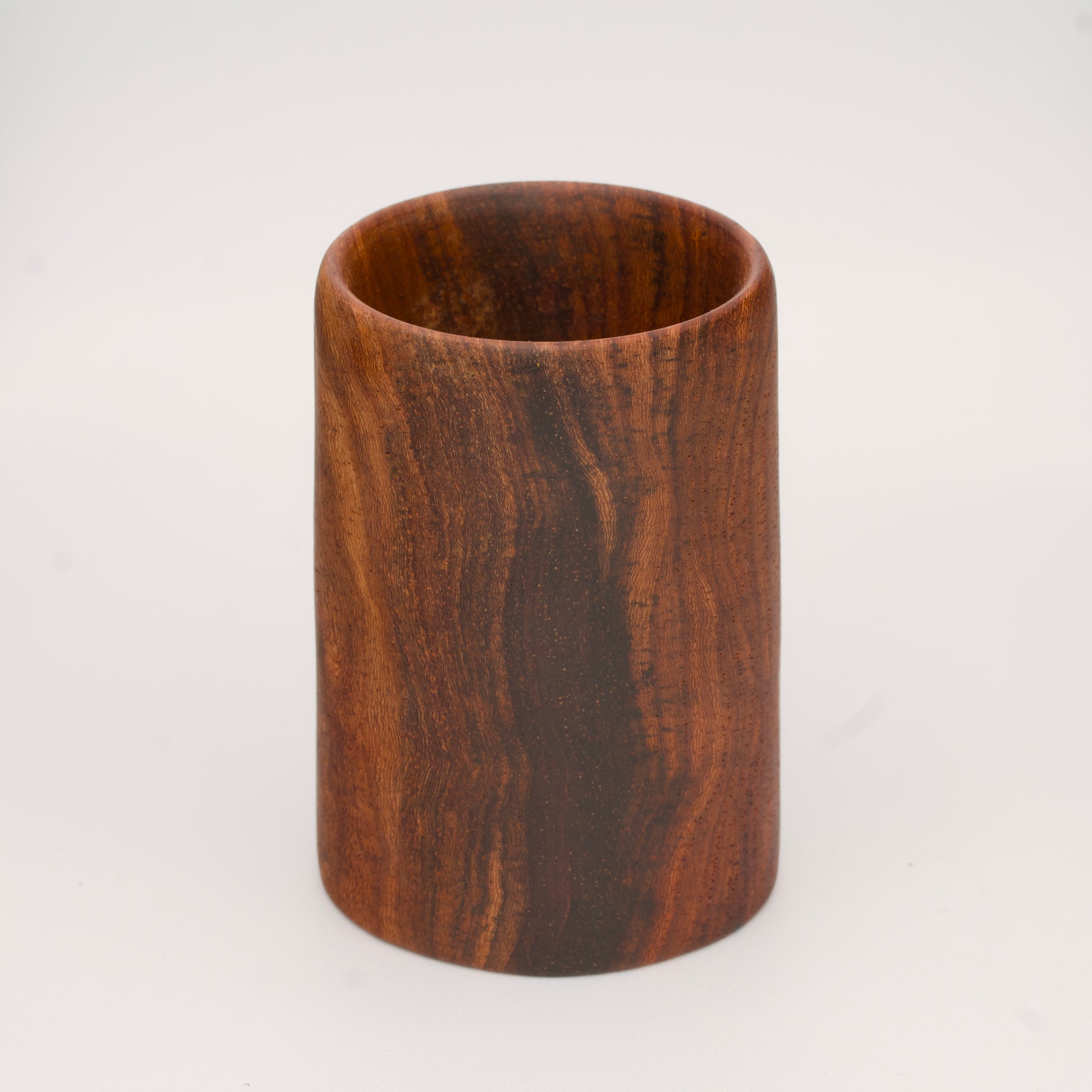 wooden shot glass with deep chocolate tones with light brown stripes on a light wooden background