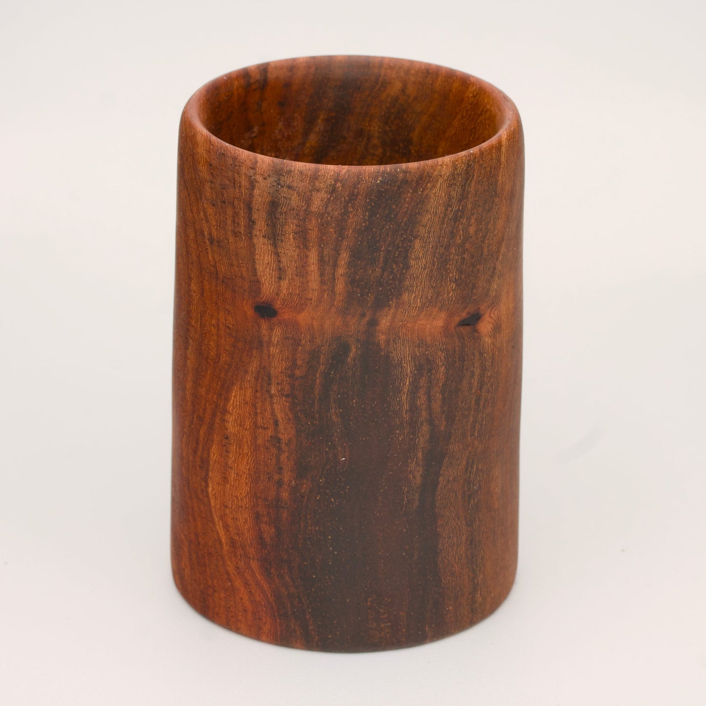 wooden shot glass with deep chocolate tones with light brown stripes on a light wooden background