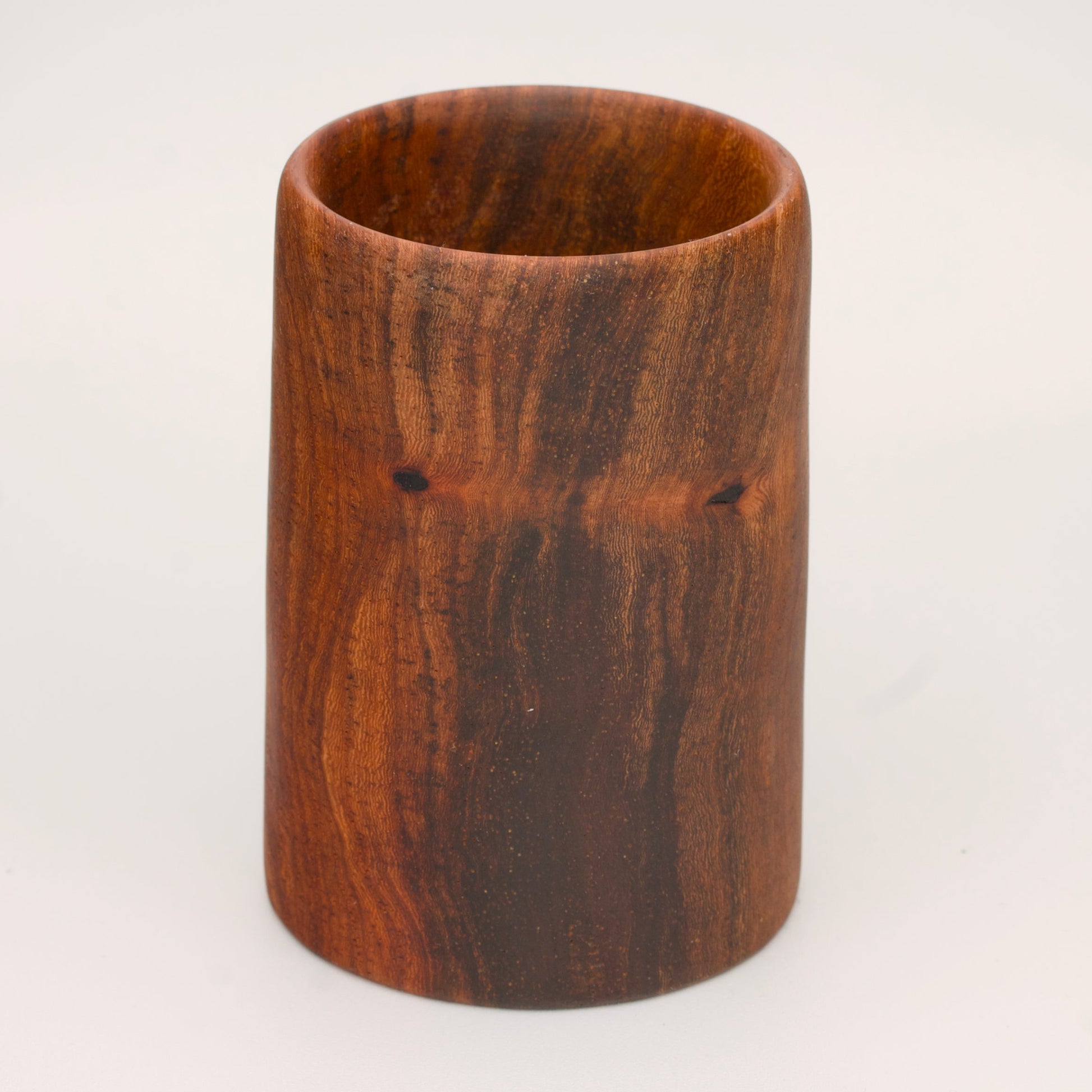 wooden shot glass with deep chocolate tones with light brown stripes on a light wooden background