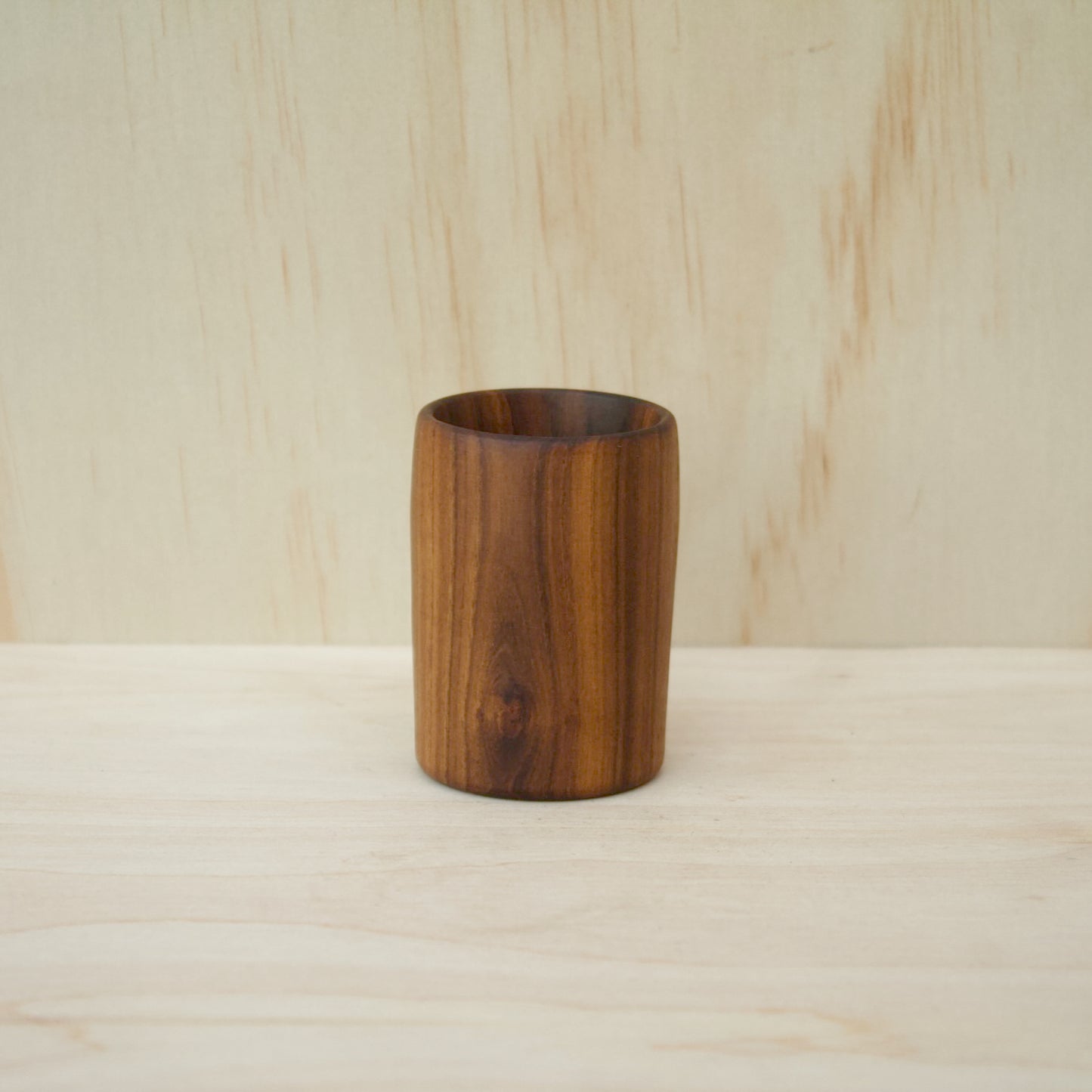 rich chocolate brown wooden cup on a light wooden surface. pattern consists of light and dark wooden stripes. 