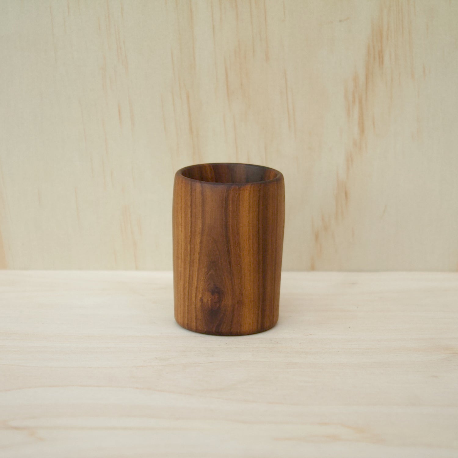 rich chocolate brown wooden cup on a light wooden surface. pattern consists of light and dark wooden stripes. 