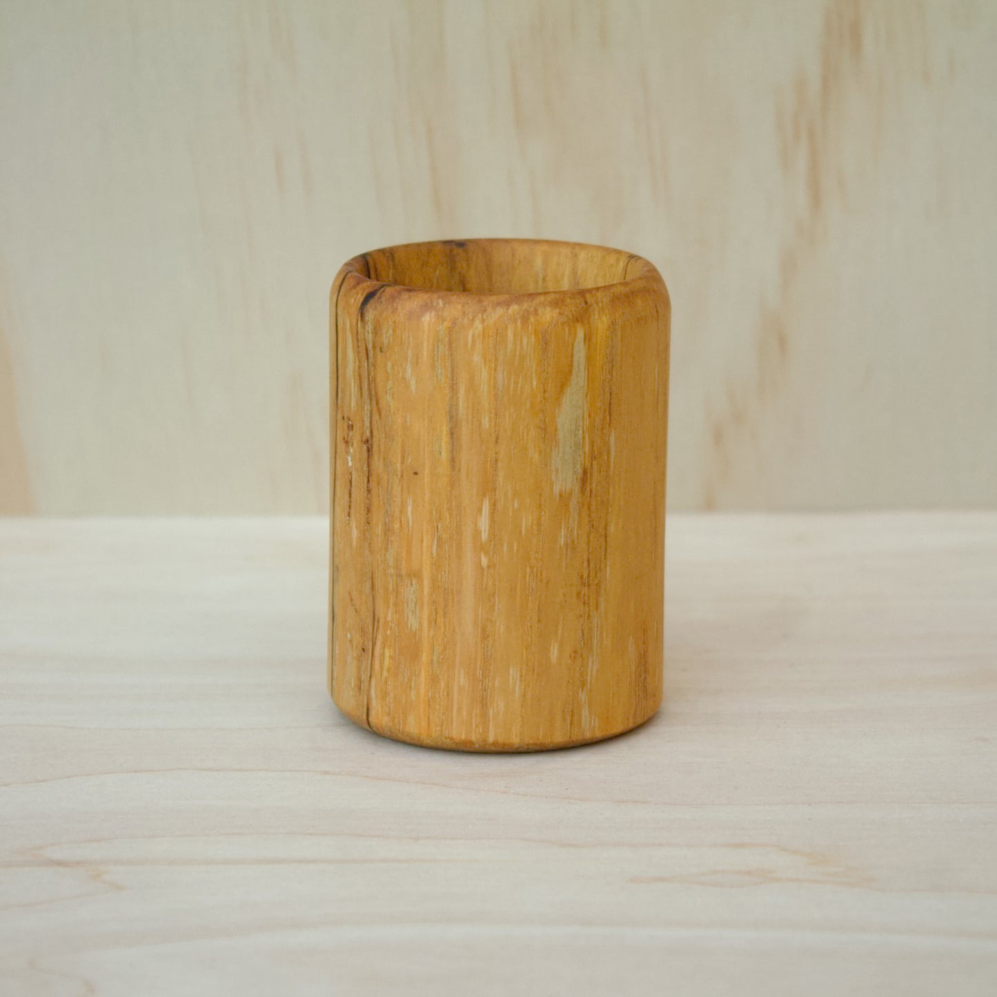 yellow wooden cup with back and white markings like a banana slug- object is hand made out of spalted hickory wood
