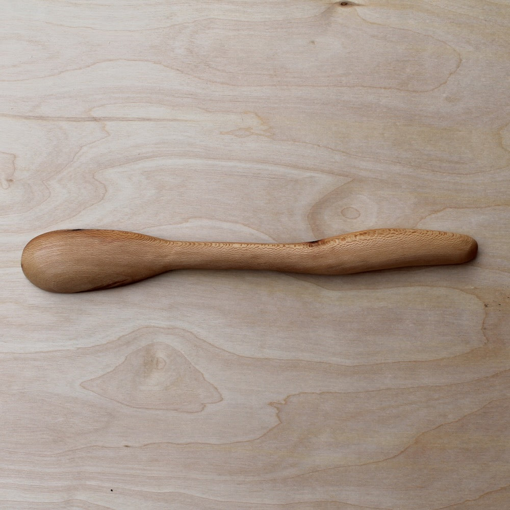 back of a hand made wooden spatula on a light wooden surfae
