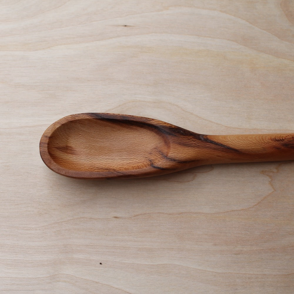 head of a light wooden spatula with a dark wooden stripe, made with sycamore wood on a light wooden background