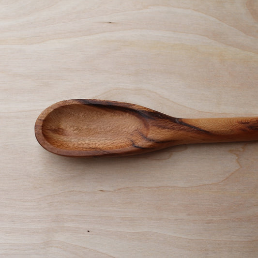 head of a light wooden spatula with a dark wooden stripe, made with sycamore wood on a light wooden background