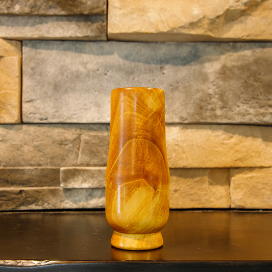 Front view of The Scholar hand-turned White Mulberry Glencairn shot glass, showing a glossy golden-amber finish, sweeping curved grain, and a pale cream figure rising from the lower body.