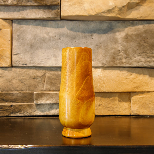 The Scholar White Mulberry Glencairn shot glass from another side, showing a lustrous honey-gold surface with broad flowing grain arcs and darker amber figure around the upper body.