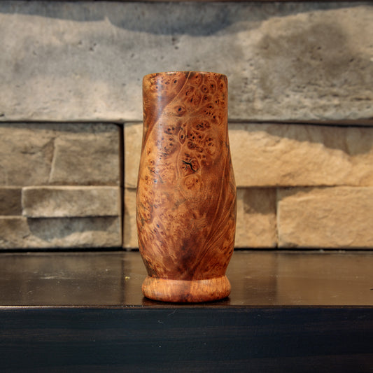 Handcrafted Amboyna burl wooden shot glass with richly contrasting reddish-brown and golden-brown tones, densely clustered burl eyes, and dark swirling grain across its rounded body.
