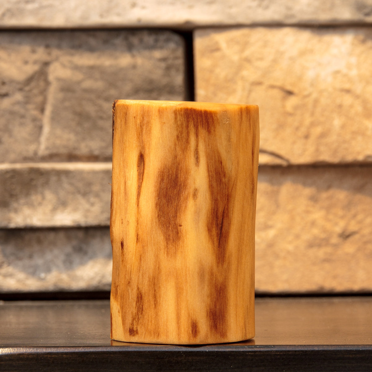 Side view of The Wild Branch cottonwood shot glass showing warm golden wood with elongated reddish-brown grain markings.