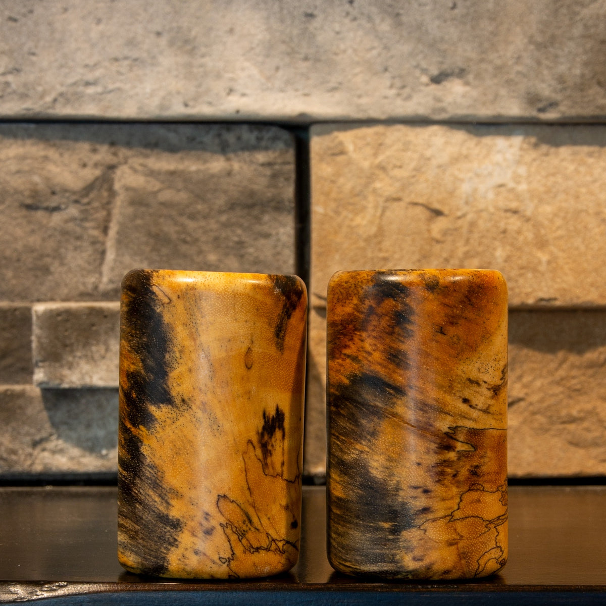 The Comic Duo wooden shot glass pair showing contrasting golden grain, dark spalting, and fine natural linework