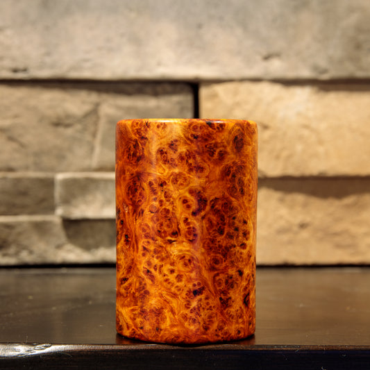 Hand-turned Amboyna burl wooden shot glass standing upright, with dense dark burl eyes throughout its glowing amber-orange exterior.