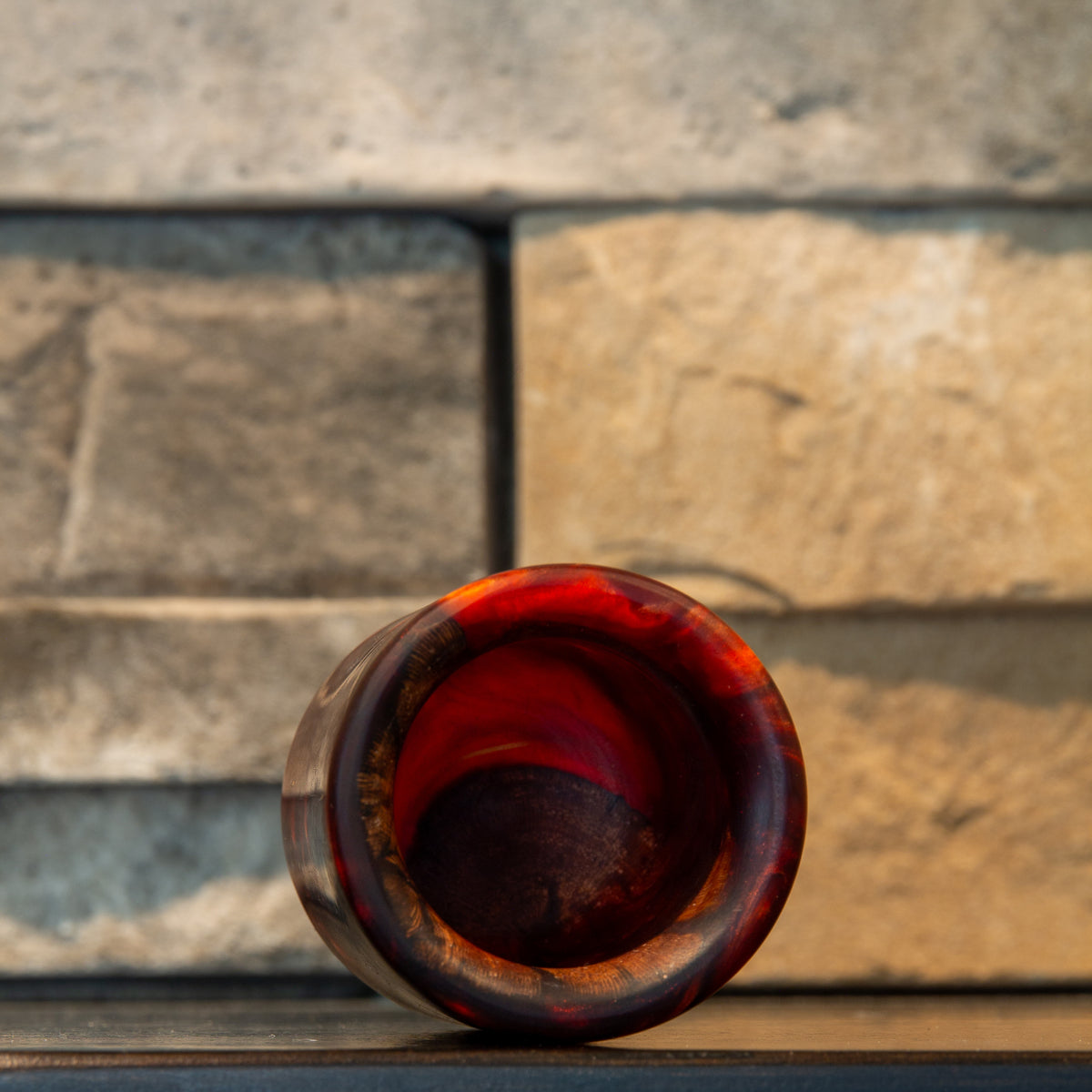 Angled view into grapevine and wine-red resin shot glass showing the circular opening, rounded rim, red interior wall, and dark wood at the bottom