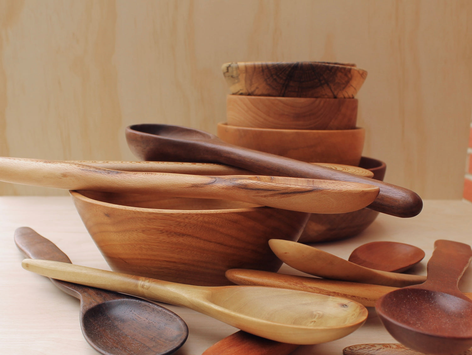Sets of hand crafted wooden bowls and spoons on a light wood background. 