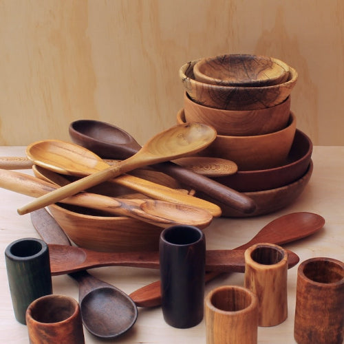 Collection of wooden kitchen utensils including bowls, spoons, and cups on a light background